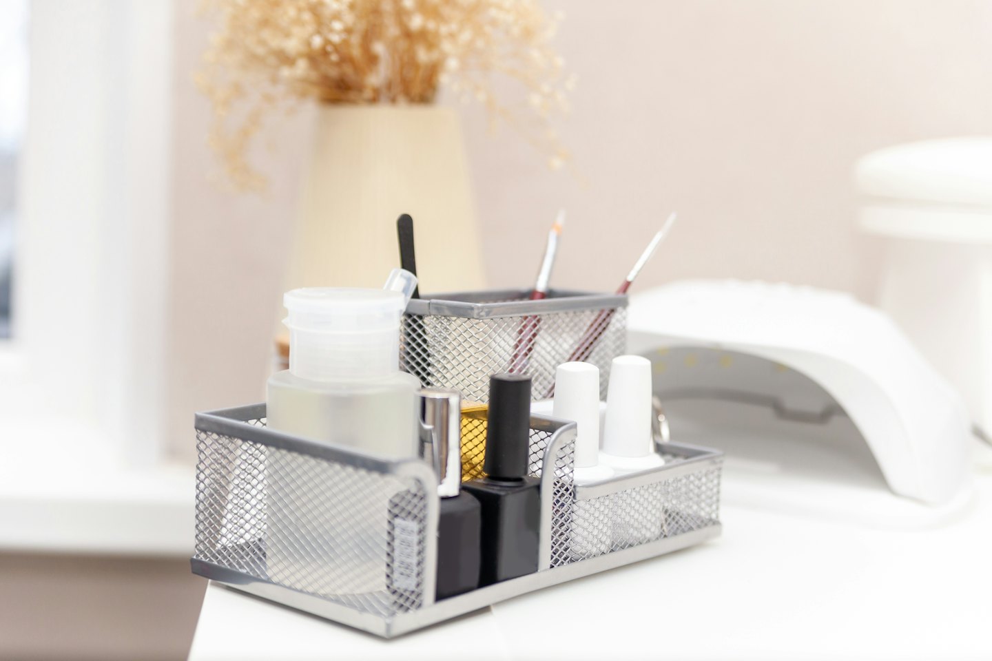 Metal mesh organizer filled with assorted nail art supplies on a table.