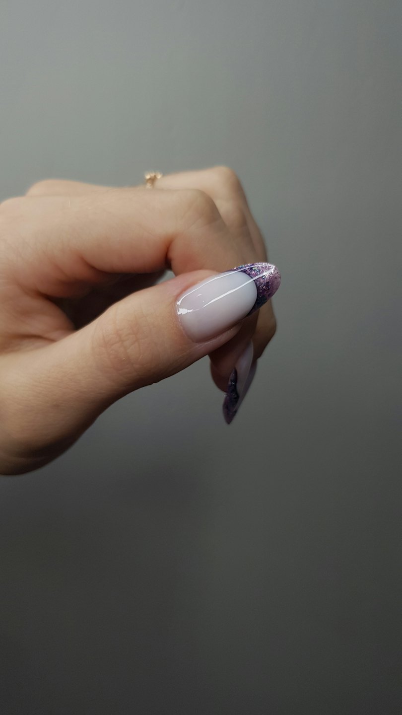 A hand displays manicured nails with white tips and purple glitter.