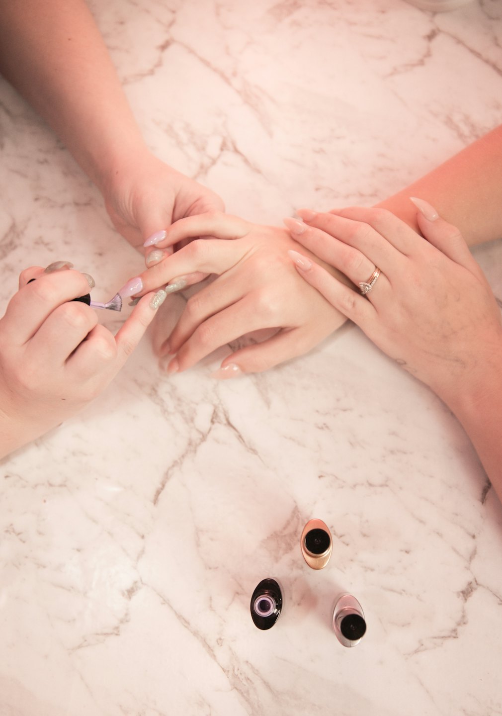 Nail technician applies glitter polish to pink acrylic nails.