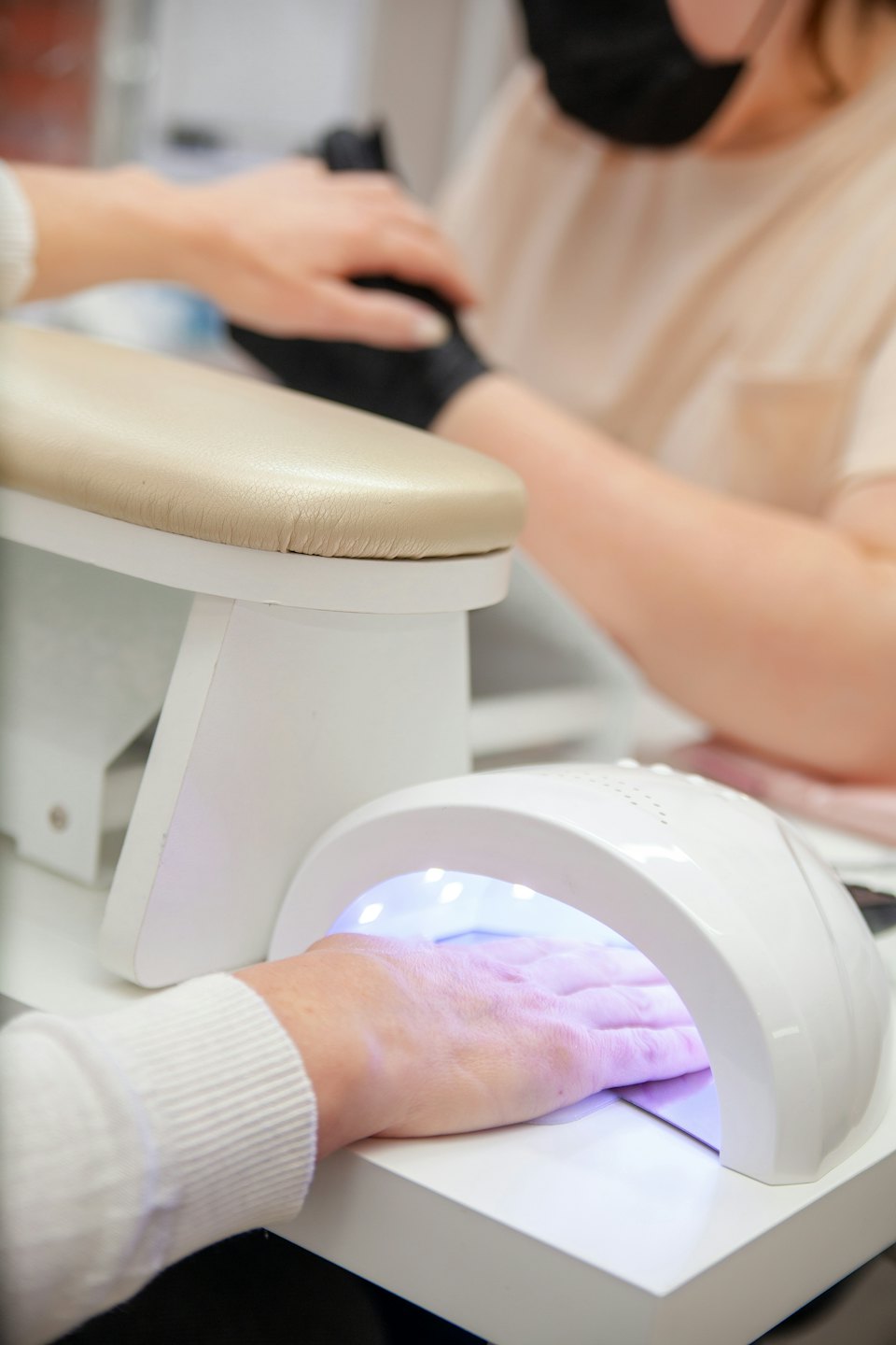 Nail technician curing gel polish under a UV lamp.