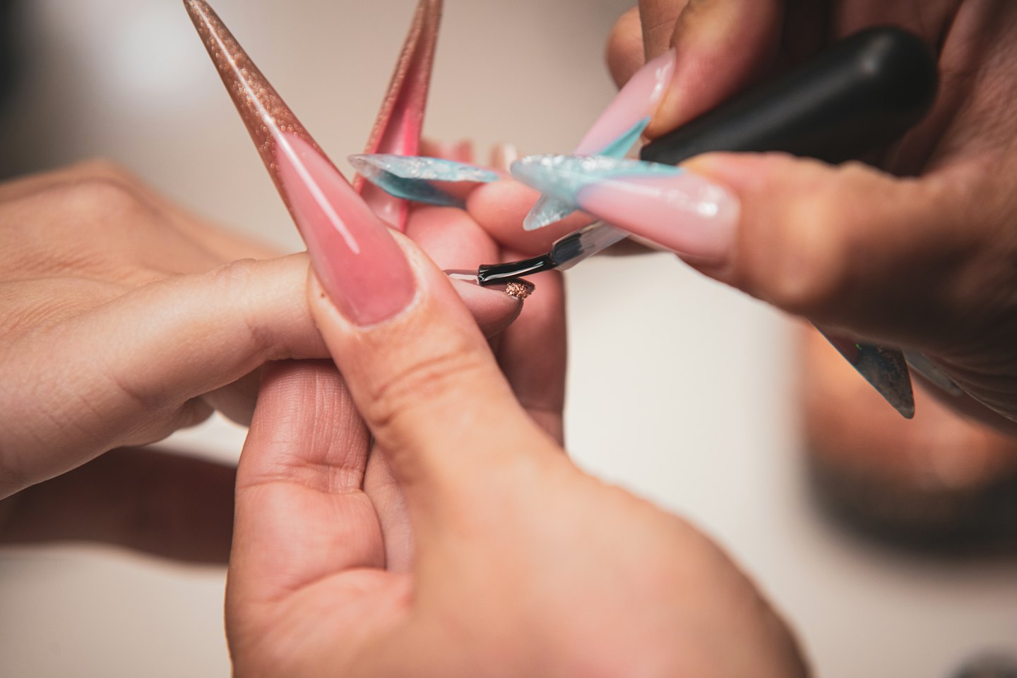Manicurist applying a glitter topcoat to a customer's fingernail.