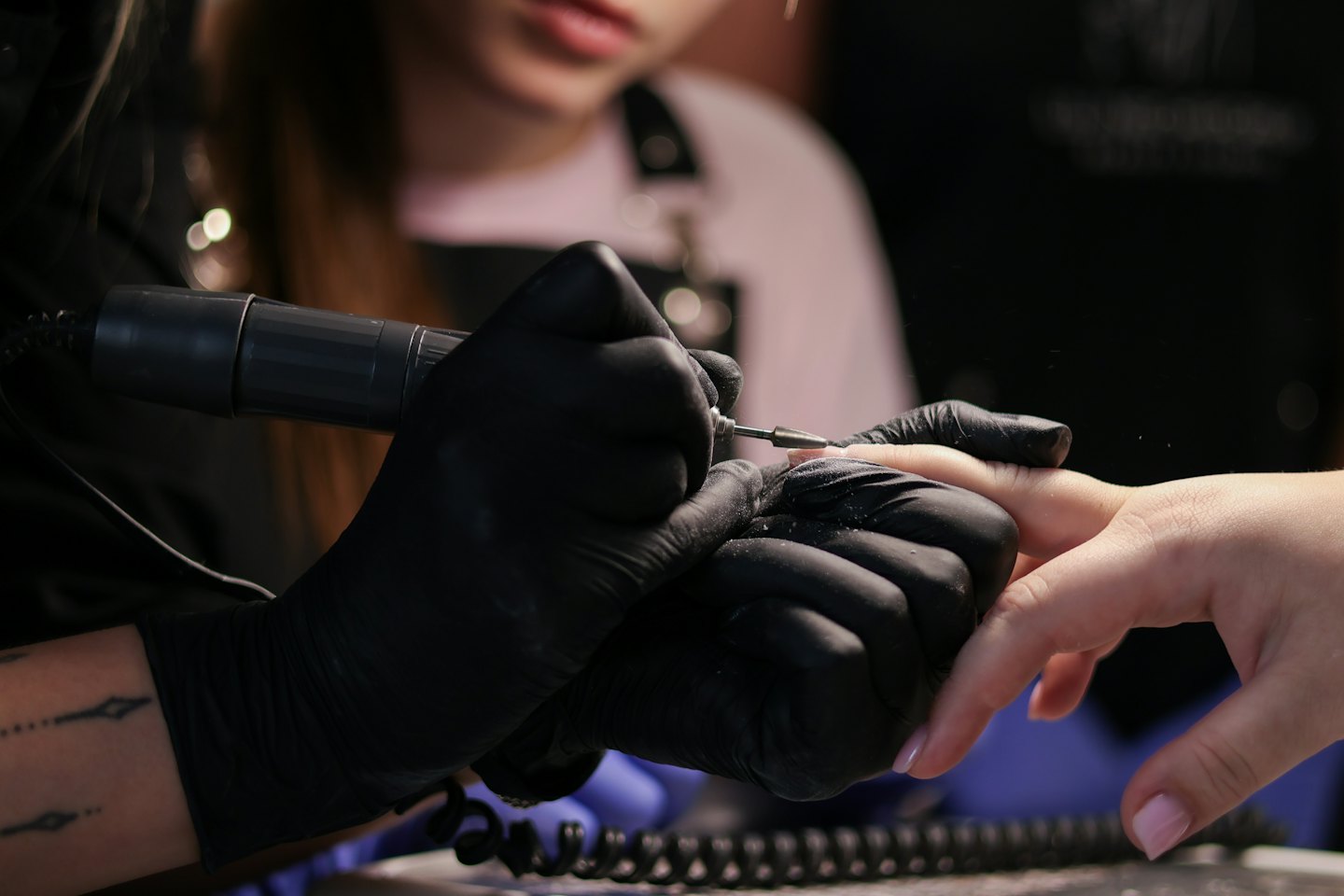 Nail technician files client's fingernails with an electric file.